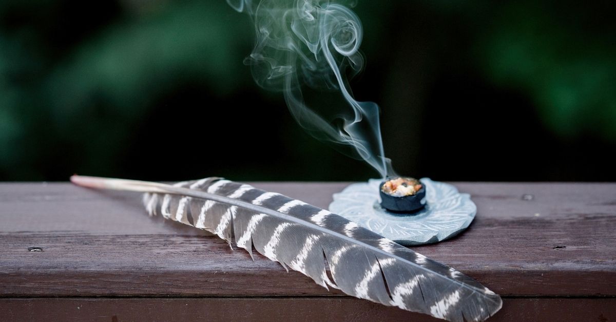 A feather lays next to a burning candle