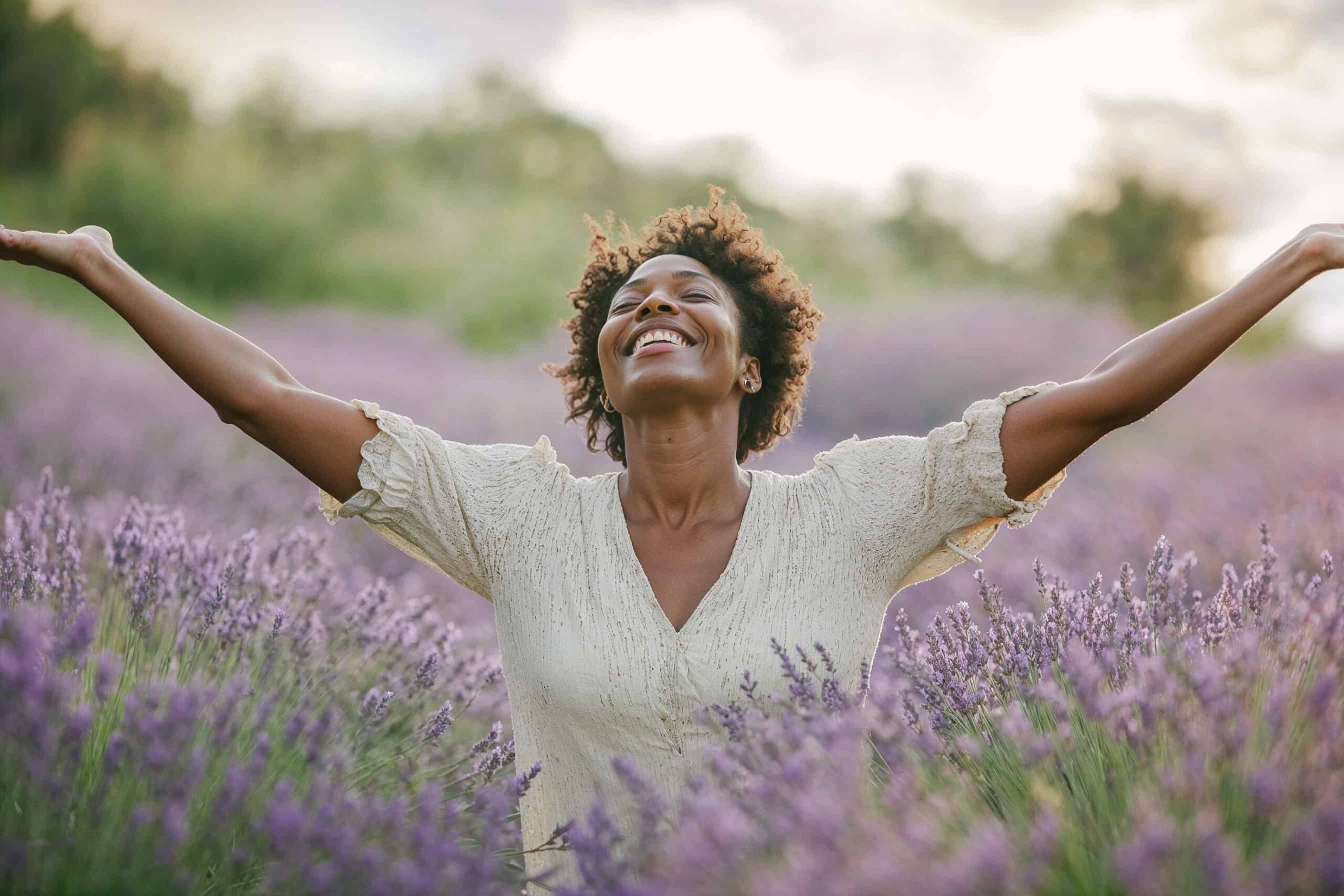 Woman with arms open wide standing in a field of lavender smiling, feeling free