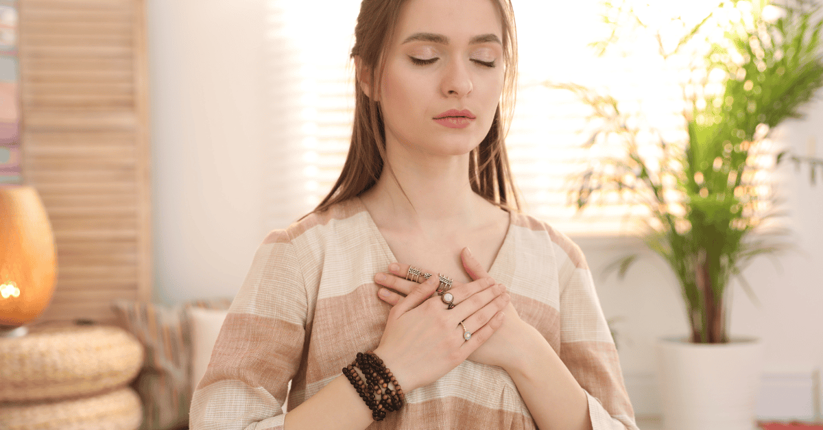 Woman in a serene, thoughtful pose with her hands on her heart doing breathing exercises.